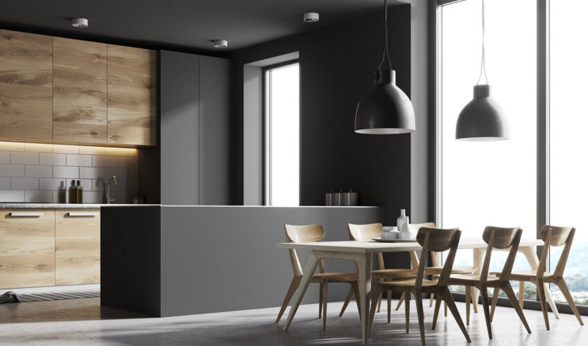 Modern kitchen with wooden cabinets, white table, six chairs, and pendant lights, featuring large windows and natural light.