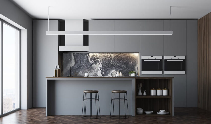 Modern kitchen with gray cabinets, marble backsplash, island with stools, and sleek built-in appliances.