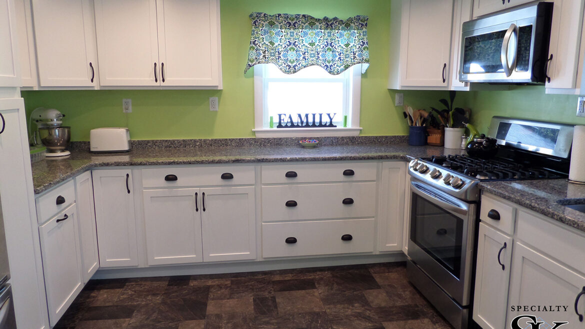 Modern kitchen with white cabinets, granite countertops, stainless steel appliances, and green walls.