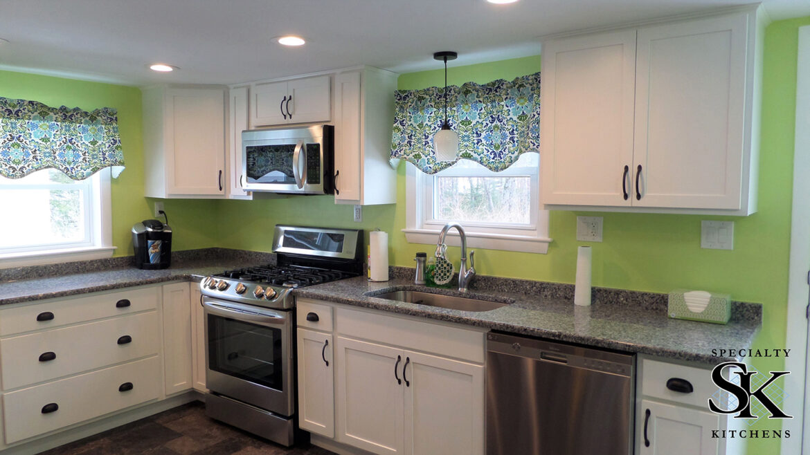 Modern kitchen with green walls, white cabinets, stainless steel appliances, patterned valances, and dark granite countertops.