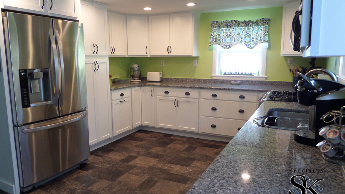 Modern kitchen with stainless steel fridge, white cabinets, green walls, and granite countertops.