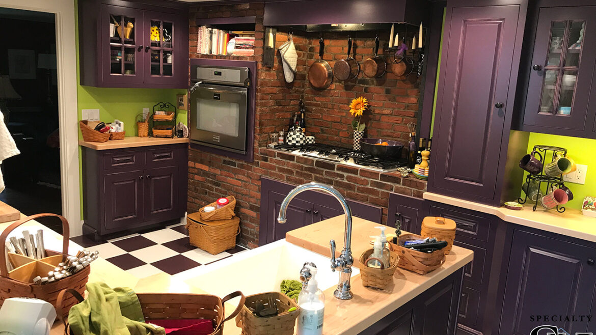 Cozy kitchen with purple cabinets, brick backsplash, vintage stove, hanging pots, and checkered floor tiles.