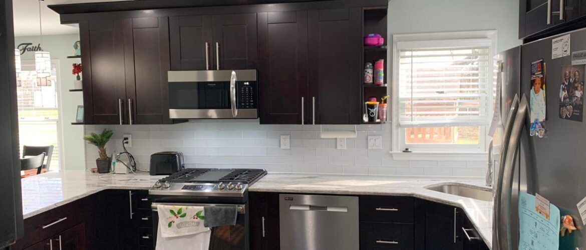 Modern kitchen with dark cabinets, stainless steel appliances, white backsplash, marble countertops, and a colorful rug.