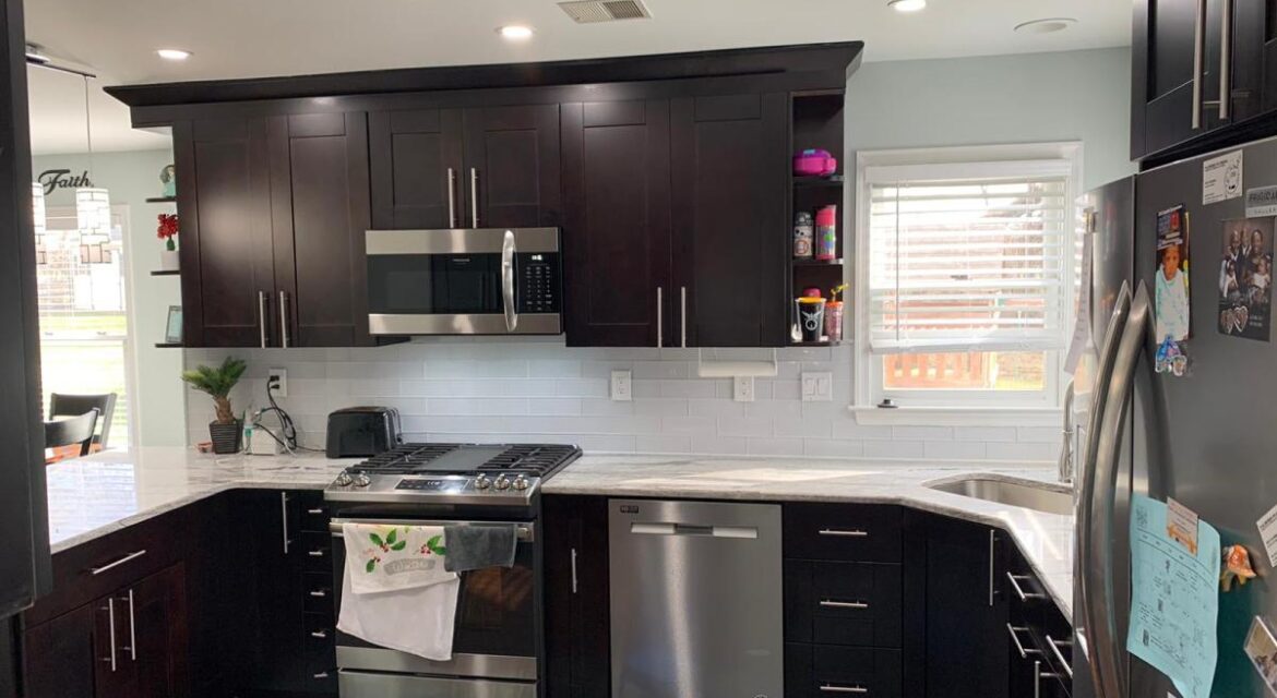 Modern kitchen with dark cabinets, stainless steel appliances, white backsplash, marble countertops, and a colorful rug.