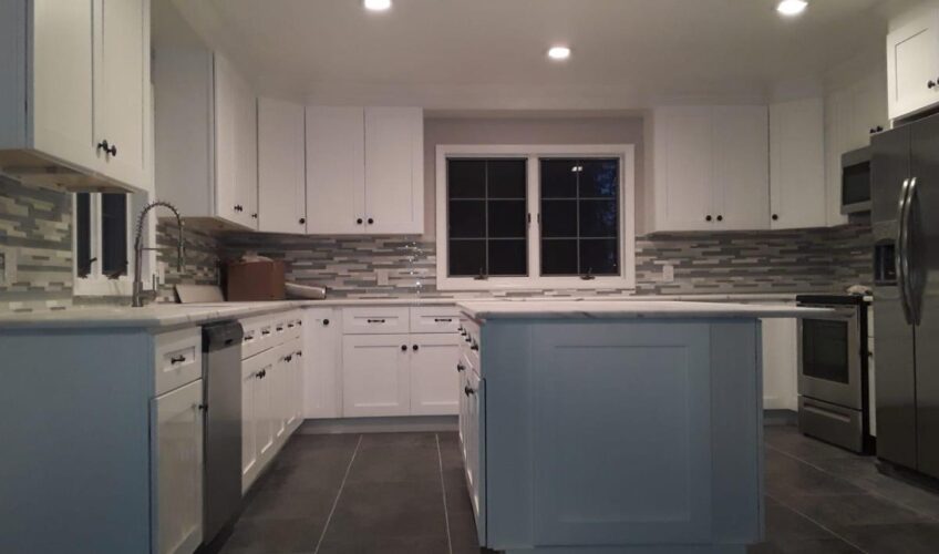 Modern kitchen with white cabinets, gray tile backsplash, stainless steel appliances, and a central island under recessed lighting.