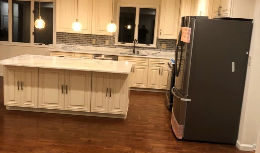 Modern kitchen with marble island, pendant lighting, stainless steel appliances, and wooden flooring.