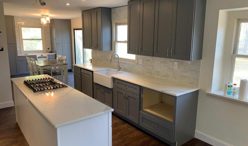 Modern kitchen with gray cabinets, white countertops, island with stovetop, and dining area in the background.