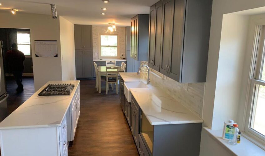 Modern kitchen with gray cabinets, white countertops, island cooktop, and dining table under soft lighting.