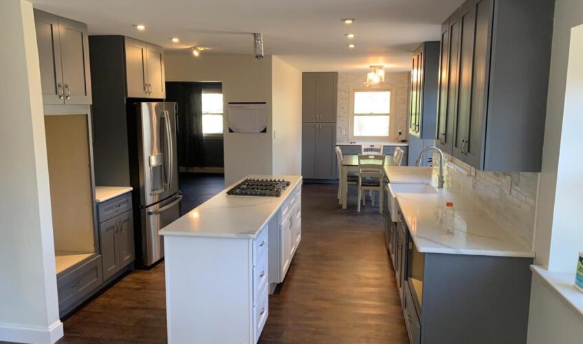 Modern kitchen with gray cabinets, white countertops, center island, gas stove, stainless steel fridge, and dining area.