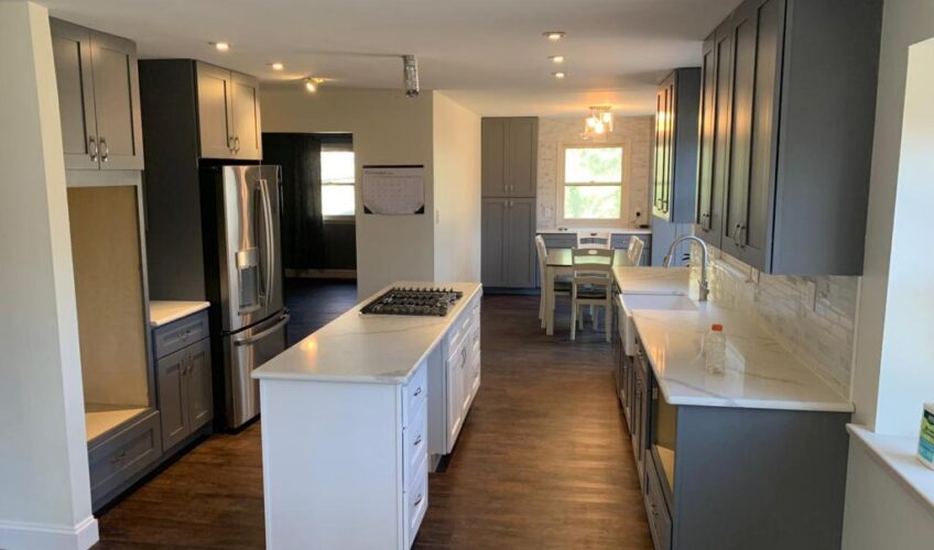 Modern kitchen with dark cabinets, white countertops, center island with stovetop, stainless steel fridge, and dining area.