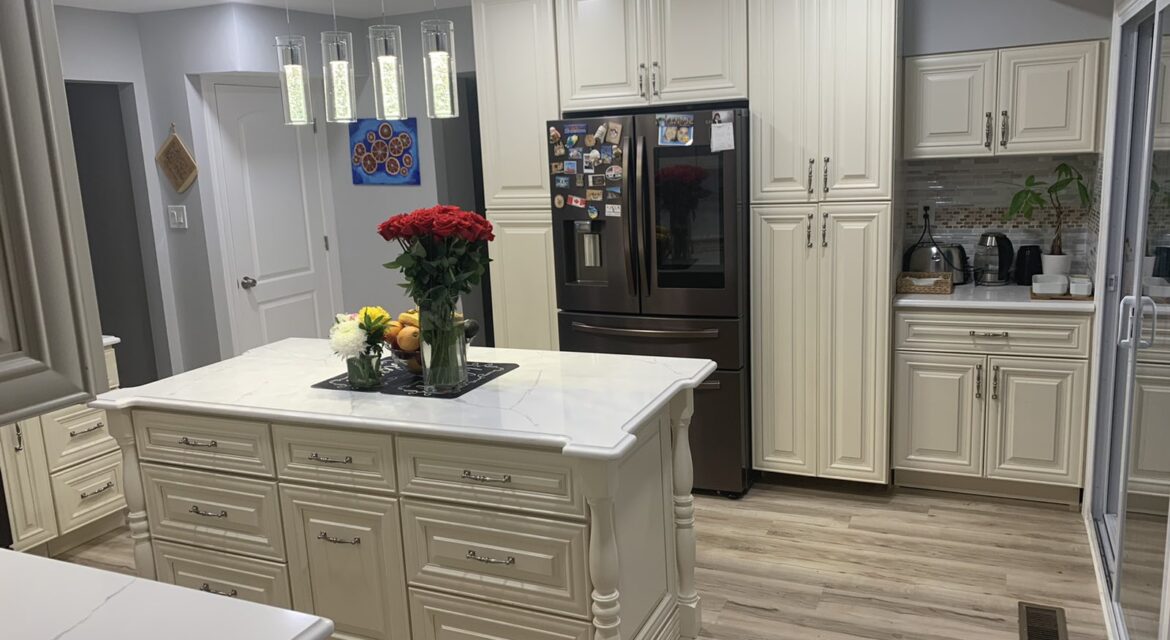 Elegant kitchen with cream cabinets, island with flowers and fruit, stainless steel fridge, and modern lighting.