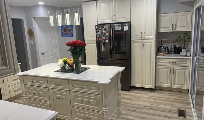 Elegant kitchen with cream cabinets, island with flowers and fruit, stainless steel fridge, and modern lighting.