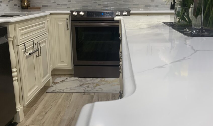 Modern kitchen with white cabinets, stainless steel appliances, marble countertops, tiled backsplash, and a vase of flowers.