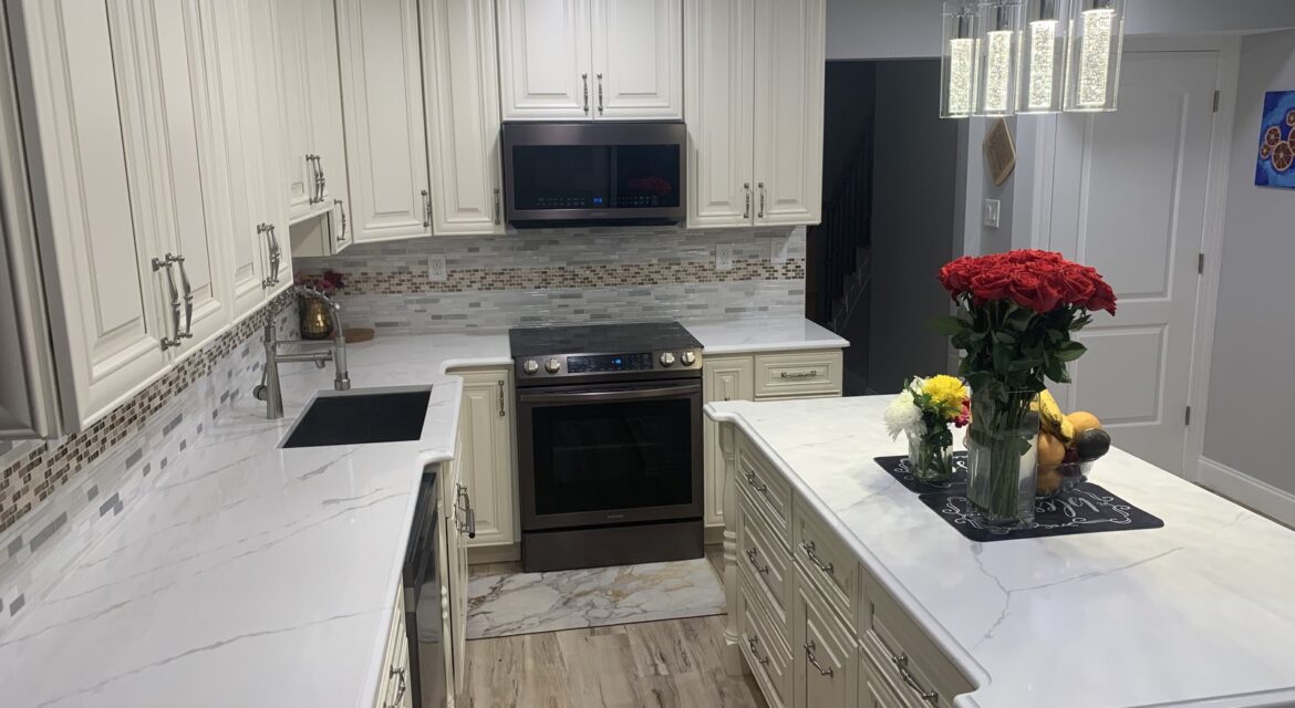 Modern kitchen with white cabinets, marble countertops, an island with flowers, and stainless steel appliances.