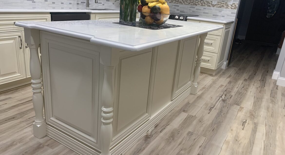 Elegant kitchen with a white marble island, fruit bowl centerpiece, and light wood flooring against a tiled backsplash.