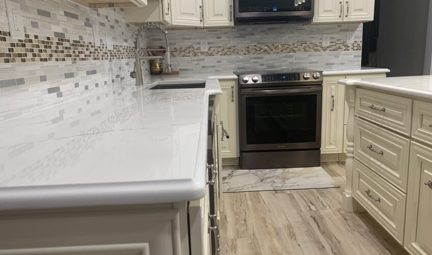 Modern kitchen with white cabinets, marble countertop, stainless steel oven, and mosaic tile backsplash.