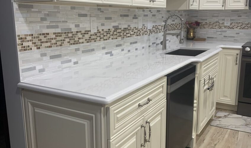 Modern kitchen with white cabinets, mosaic tile backsplash, and light wood flooring. Features a black dishwasher and silver faucet.