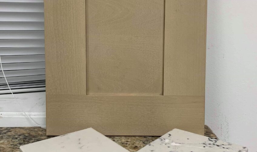 Beige cabinet door with four white marble samples on a granite countertop.